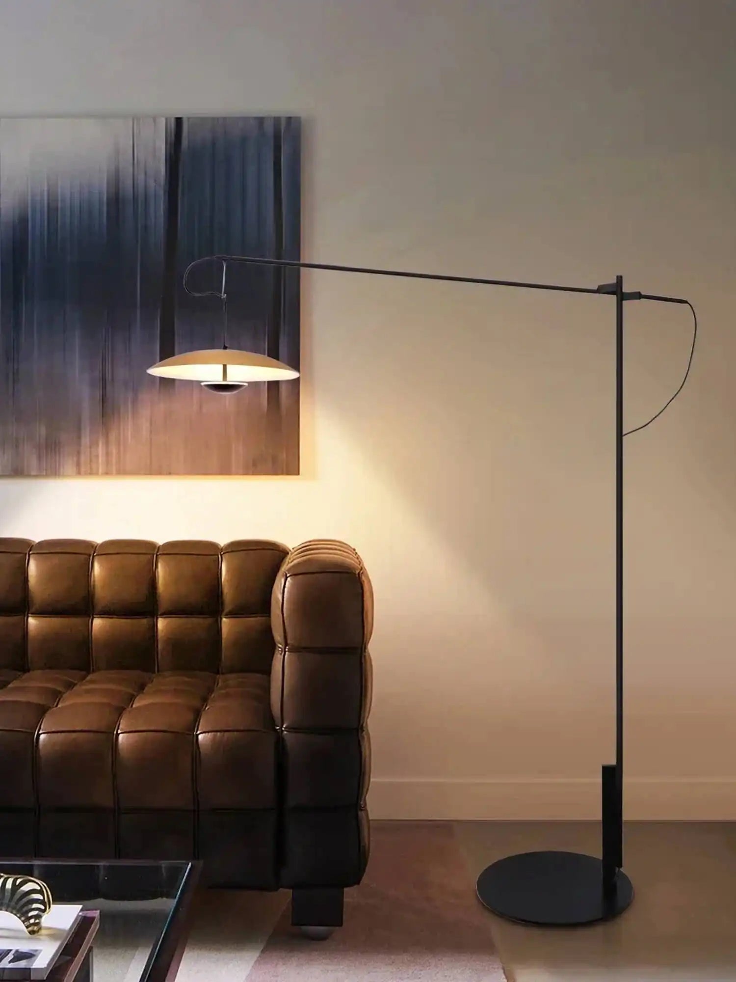 Sleek floor lamp with an adjustable arm and disc-shaped shade illuminating a leather sofa.