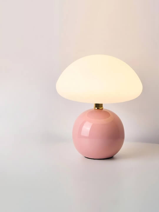 Pink ceramic table lamp with a round base and white dome shade.